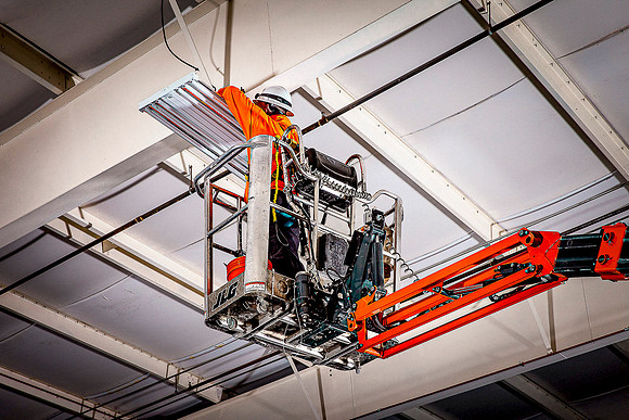 Electrian installs industrial ceiling lighting in aerospace museum.