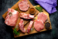 An assortment of different pork meat cuts on cutting board.