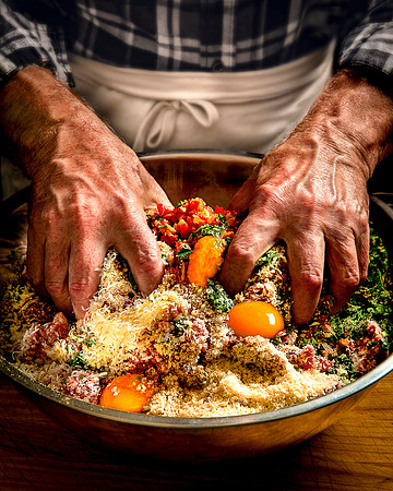Male hands are plunged into a large bowl of meatball ingredients.