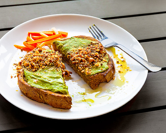 Avocado toast with chopped walnuts on a white plate.