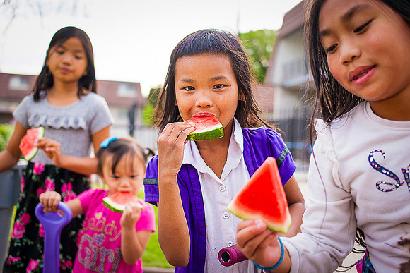 Four Asian refugee girl eating watermelon on playground.