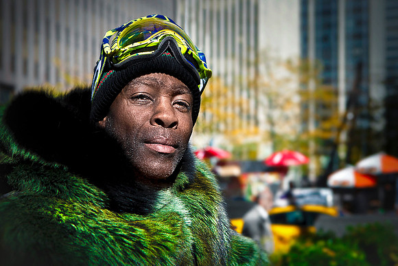 Cool black dude in Manhattan wearing green fur coat and ski goggles on warm day.