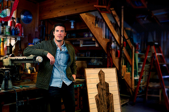 Artisan woodworker and furniture maker stands next to latest creation.