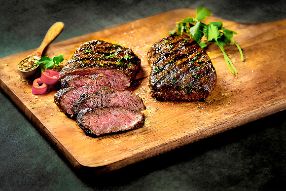Still life of two cooked ribeye beef steaks on a cutting board.