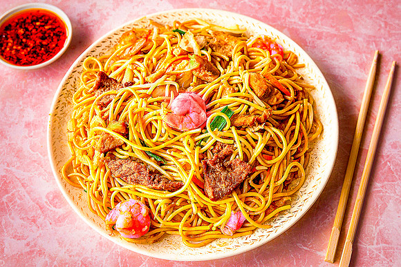 Plate of Shrimp and Pork LoMein with chopsticks on pink table.