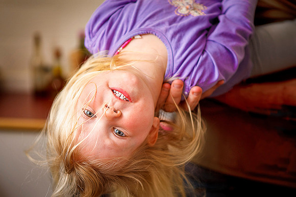 Father holds little girl Molly upside down in the kitchen.