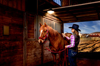 A woman horse owner in a cowboy hat brushes her horse in the stable.
