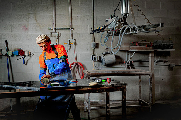 Edgar of InteriorWorx Countertops polishes a slab of granite with a rotary water polisher in the workshop.