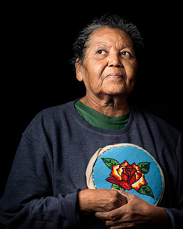 Ute tribe older woman looks afar holding handmade purse.