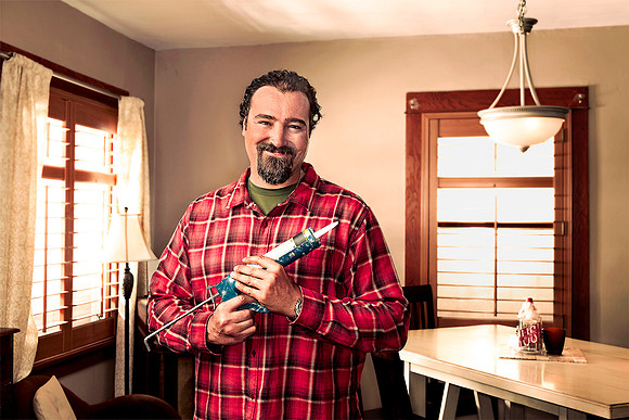 Man in living room with caulking gun ready to make repairs.