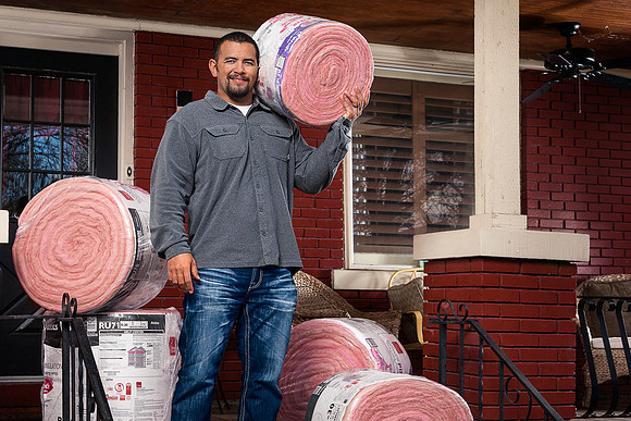 Man on front  porch with rolls of pink insulation.